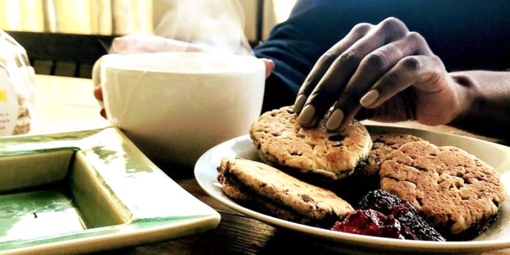 photo of a person picking up a welsh cake and drinking a hot beverage