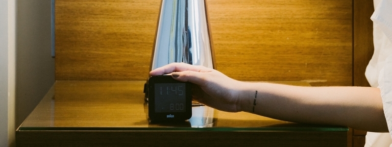 A hand reaching for an alarm clock.