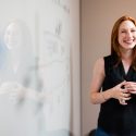 Woman is smiling and stands by whiteboard.